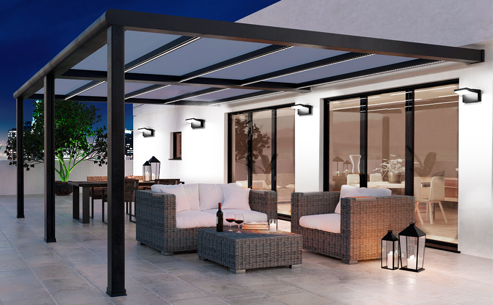 Modern outdoor patio with black metal pergola, glass roof panels, and wicker furniture. Features wall-mounted lights and lanterns, creating a cozy evening ambiance.